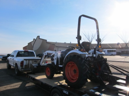 Bobcat loader on flatbed trailer pulled by a pickup
